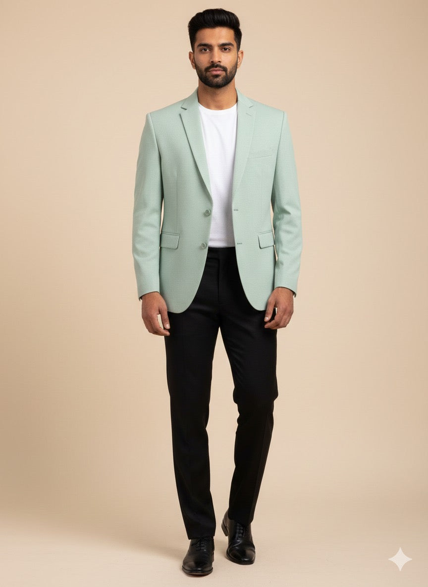 Man wearing a light green blazer over a white shirt with black pants on a beige background