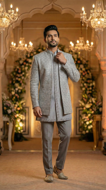 Man in a gray traditional outfit standing in an ornate room with chandeliers and floral decorations.