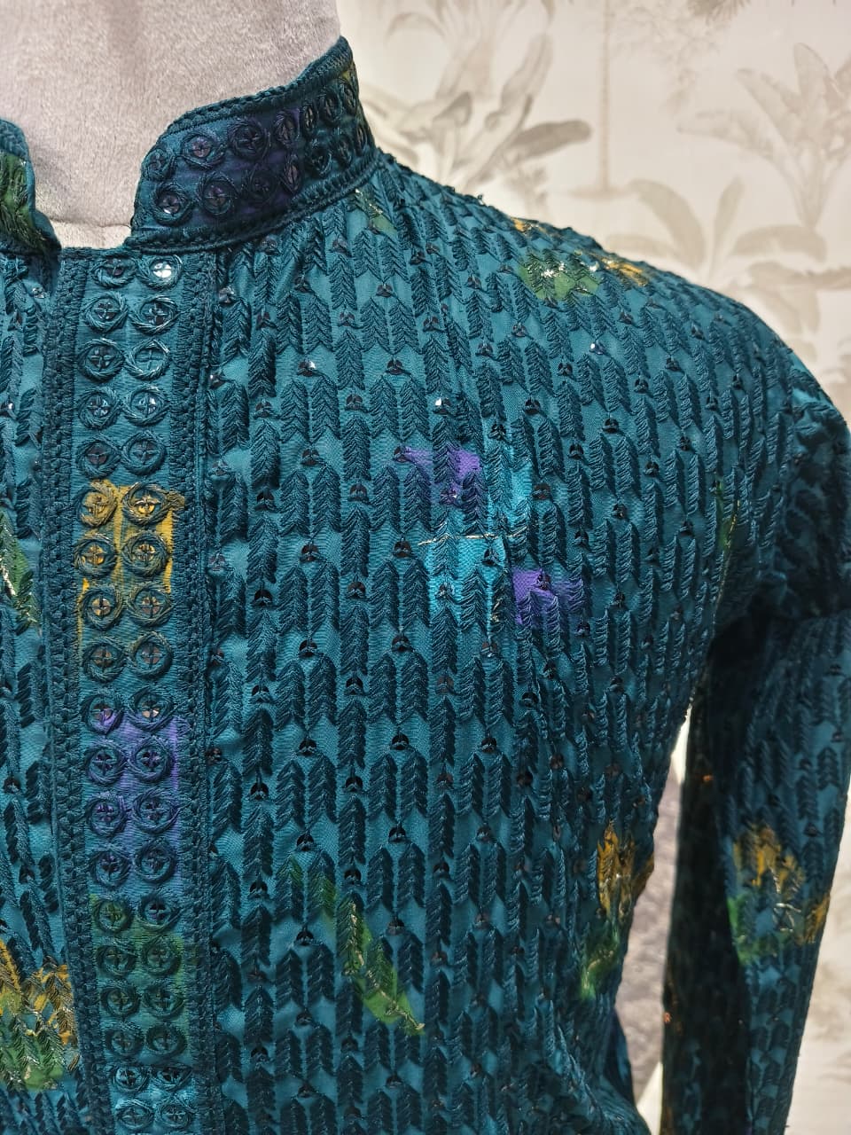 Close-up of a teal embroidered garment with floral patterns on a neutral background