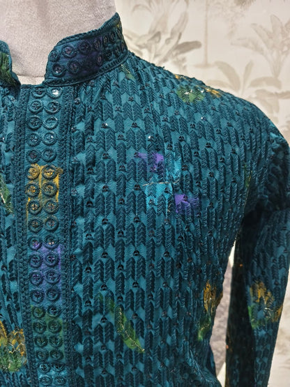 Close-up of a teal embroidered garment with floral patterns on a neutral background