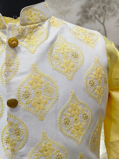 White embroidered garment with yellow patterns and buttons on a neutral background