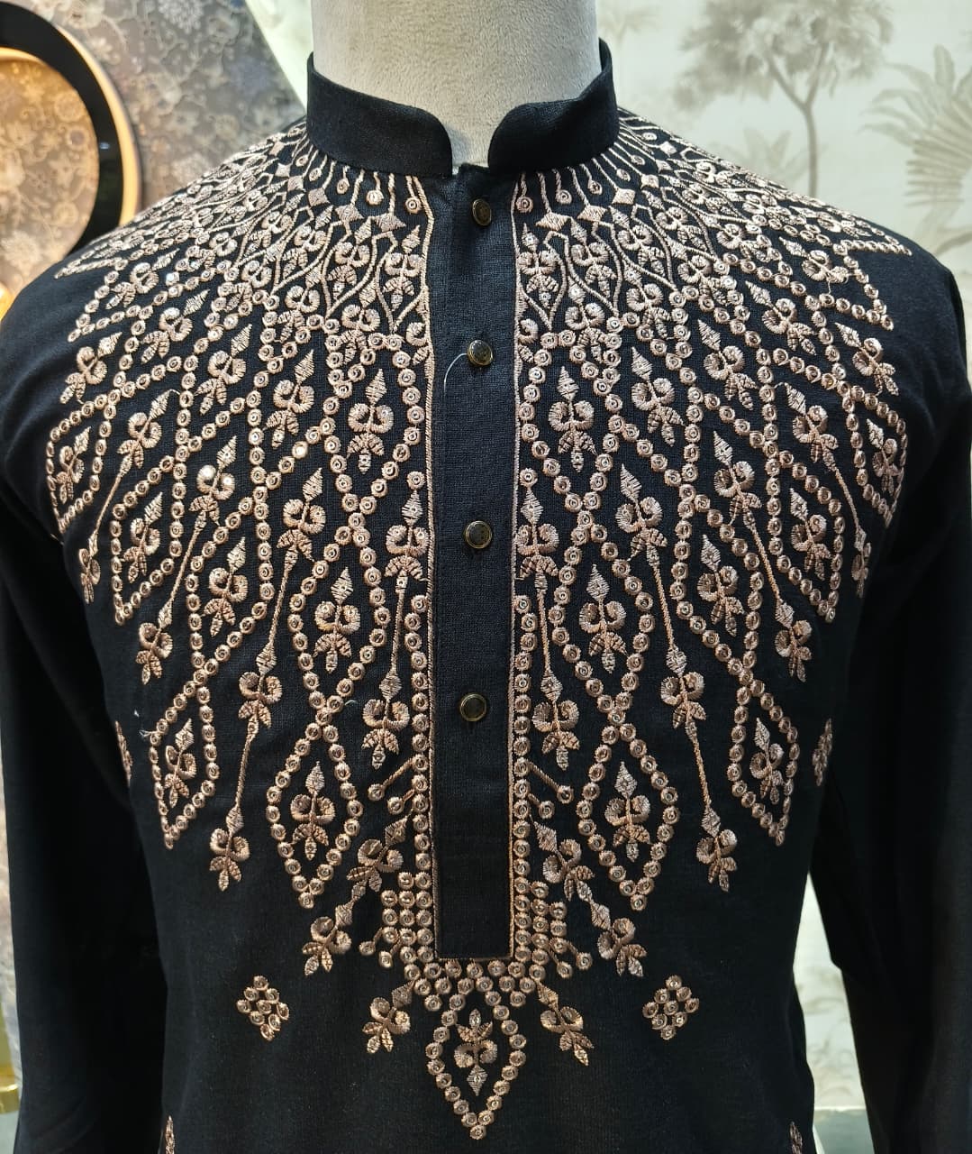 Black shirt with gold embroidery on a mannequin against a neutral background