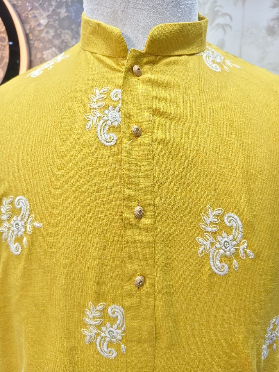 Yellow shirt with white embroidery on a mannequin against a neutral background