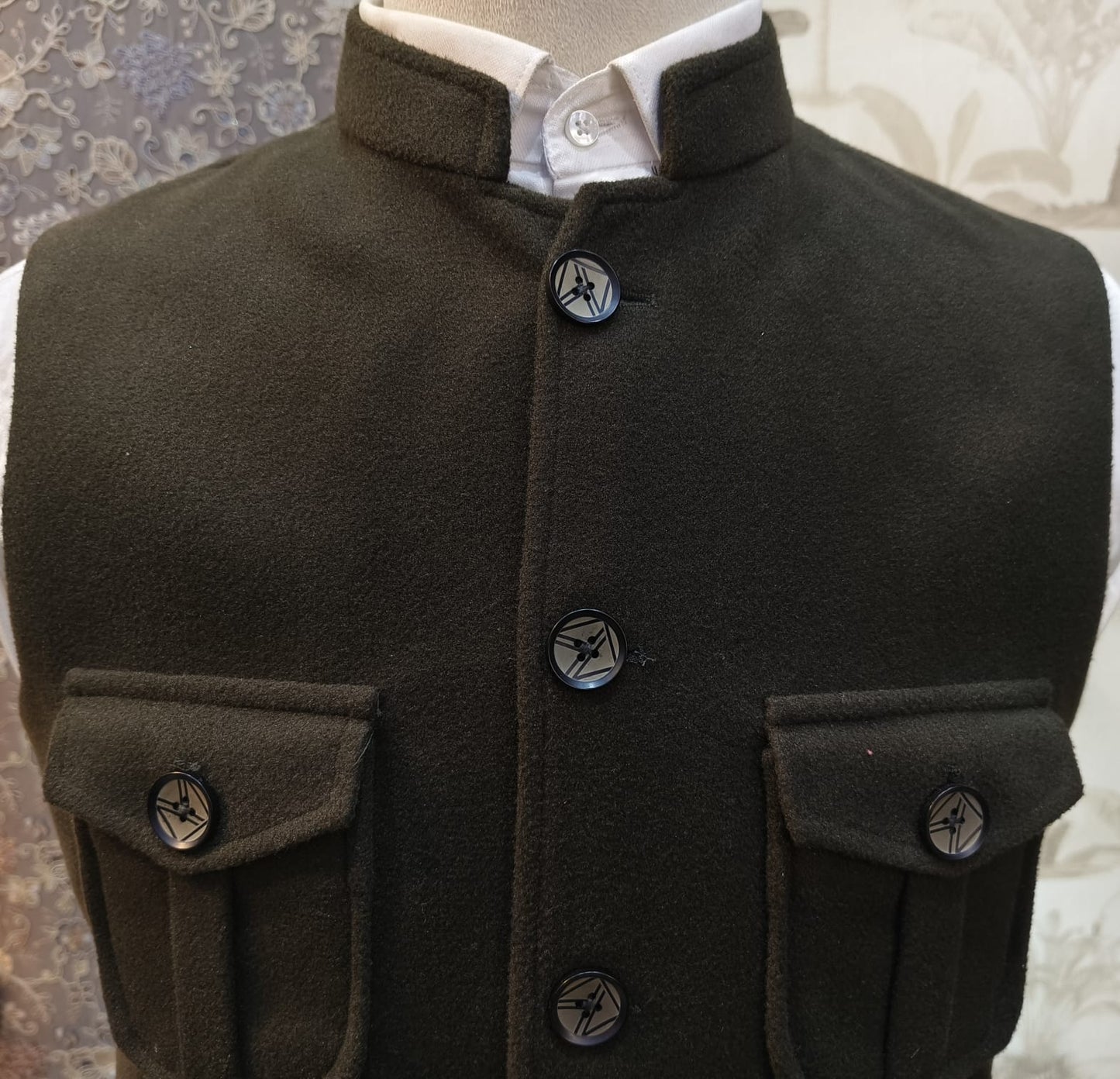 Dark green coat with button details on a mannequin against a patterned background