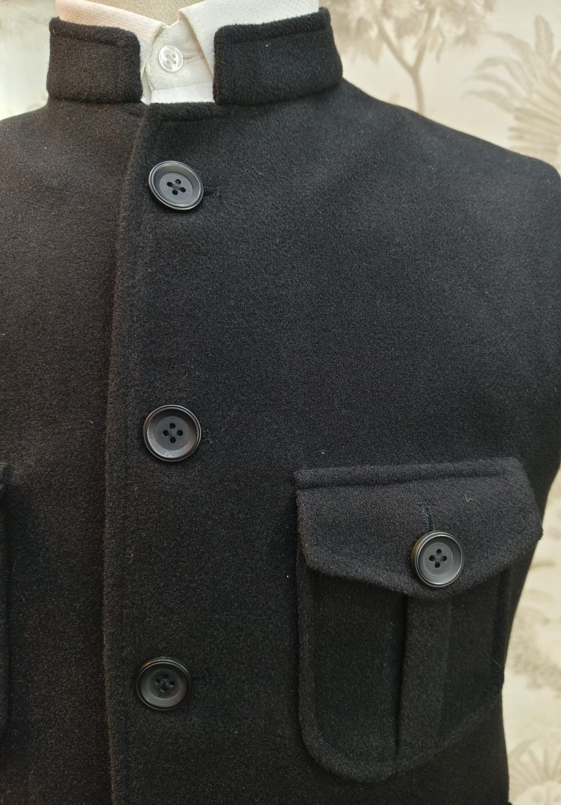 Close-up of a dark coat with buttons and a pocket on a mannequin.