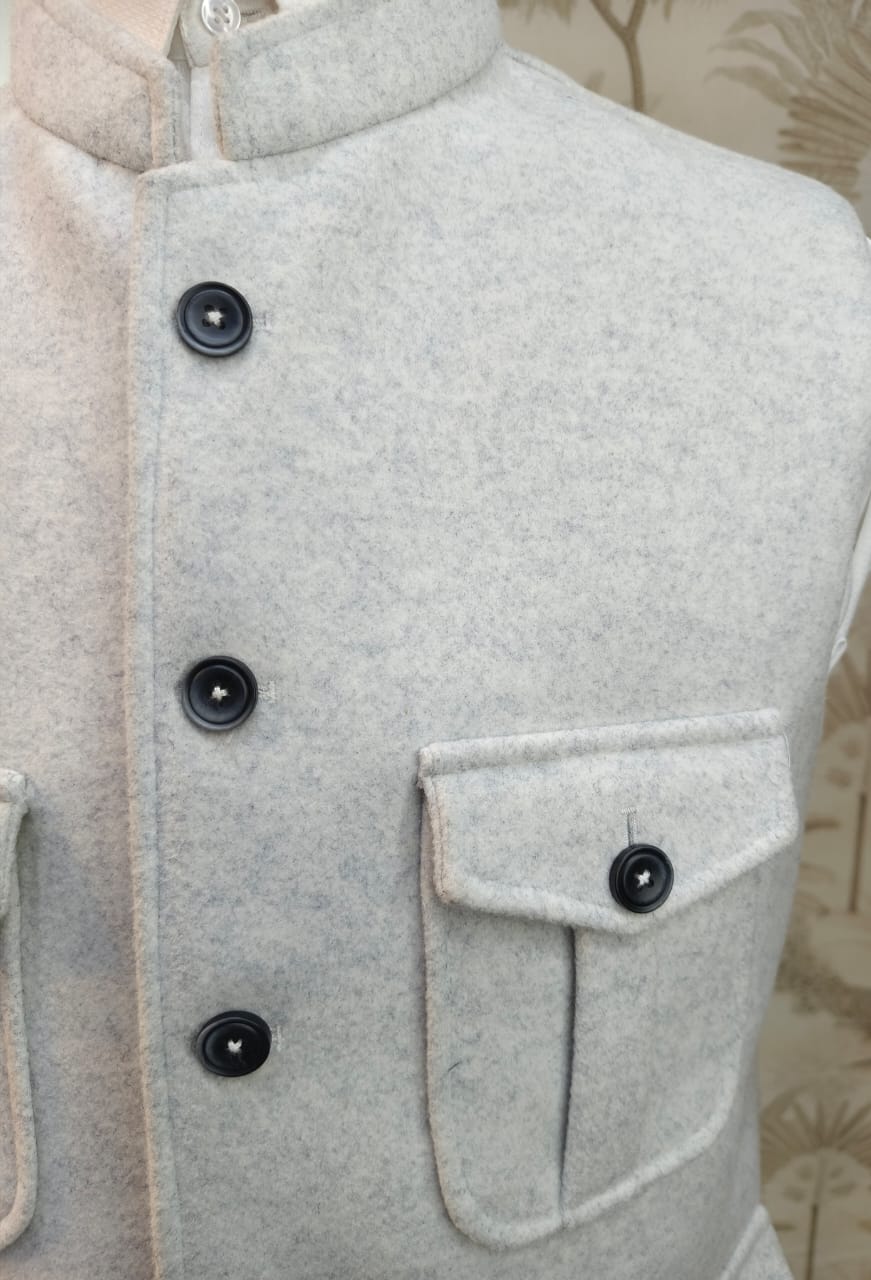 Close-up of a gray coat with black buttons and a pocket on a neutral background