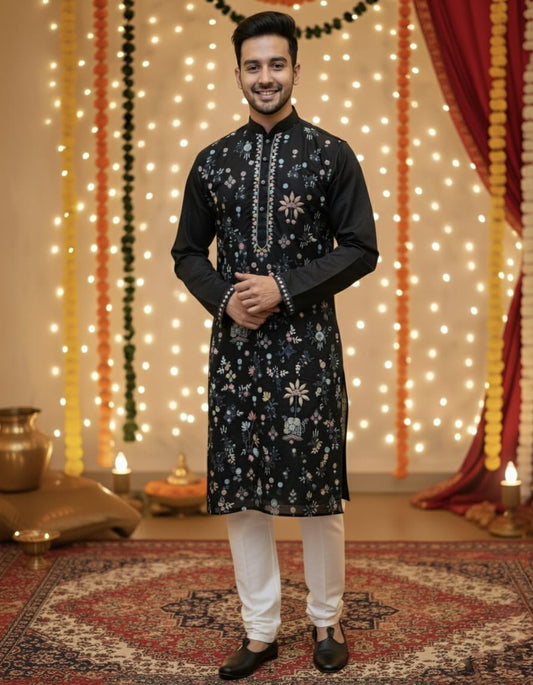 Man wearing a black embroidered kurta with white pants in a decorated room.