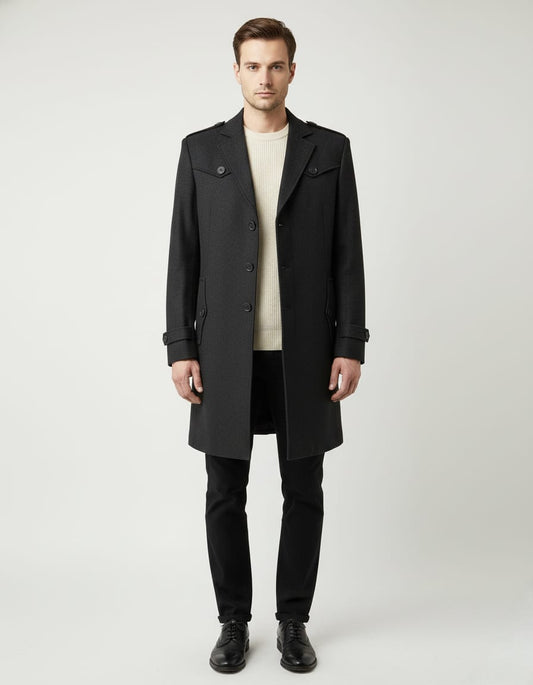 Man wearing a dark grey coat over a beige sweater and black pants on a white background